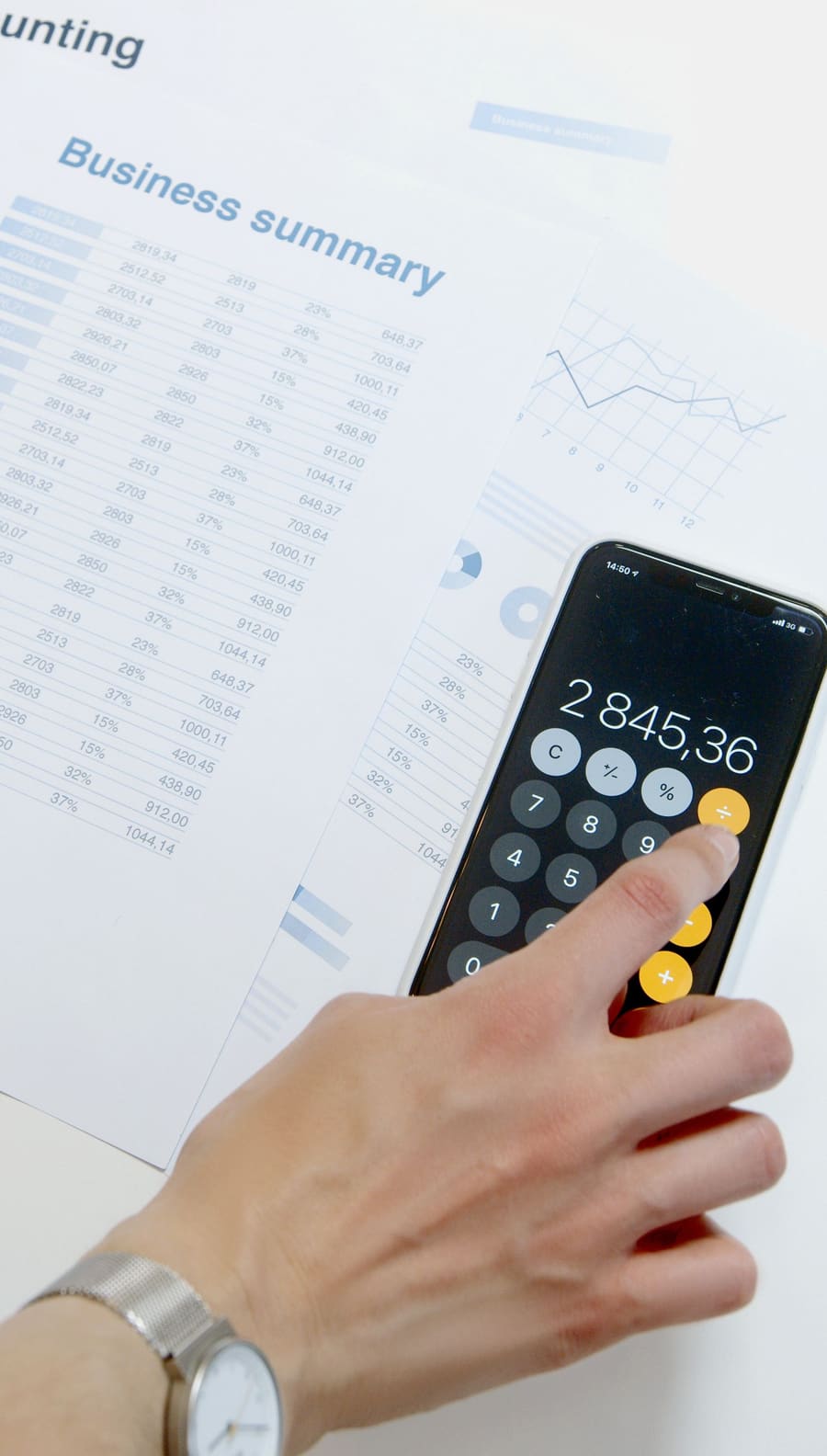 Dłoń obsługująca kalkulator na smartfonie na tle dokumentów finansowych